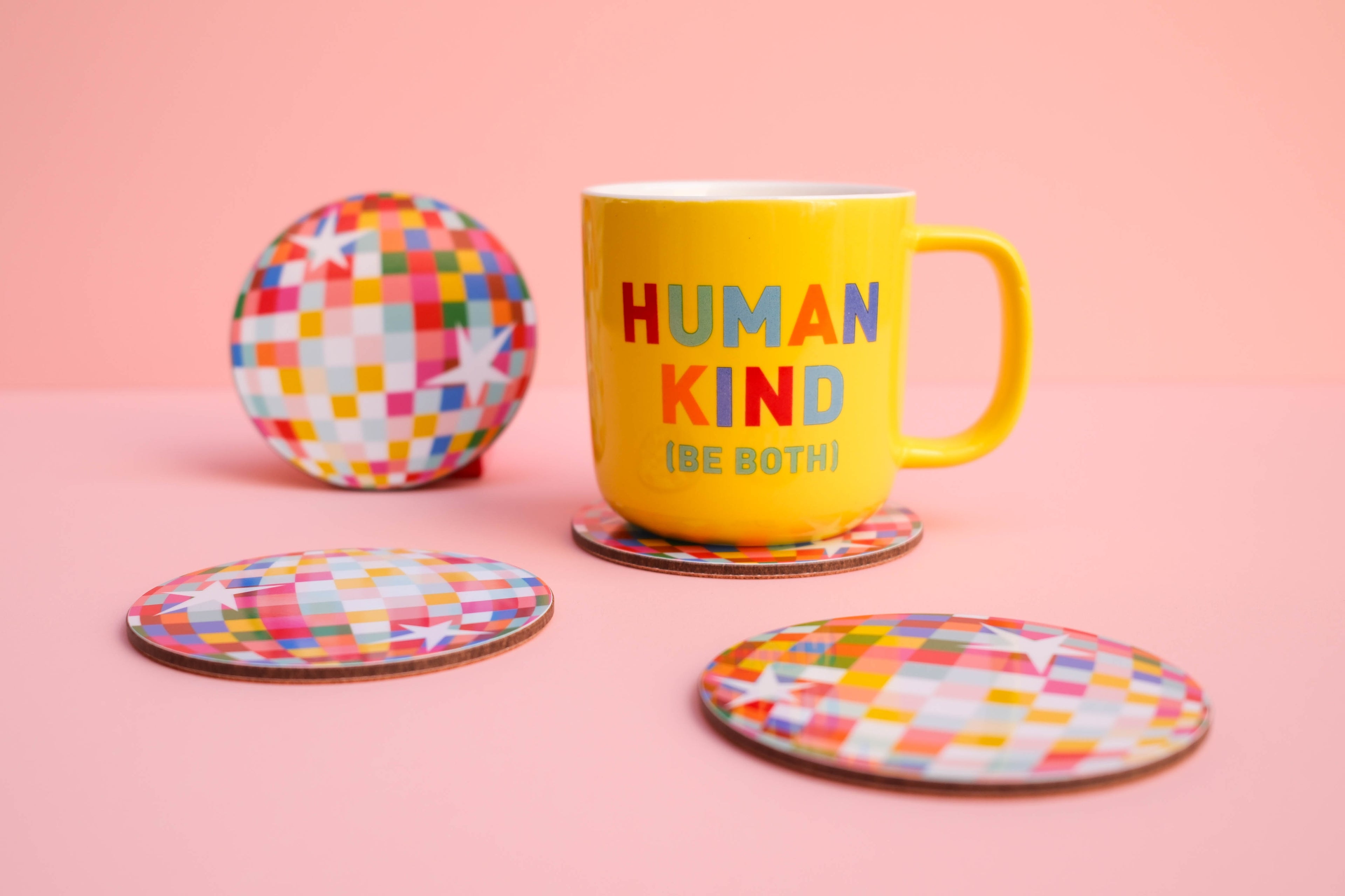 Colorful mug awith 'Human Kind (Be Both)' text, colourful disco ball coaster on pink background