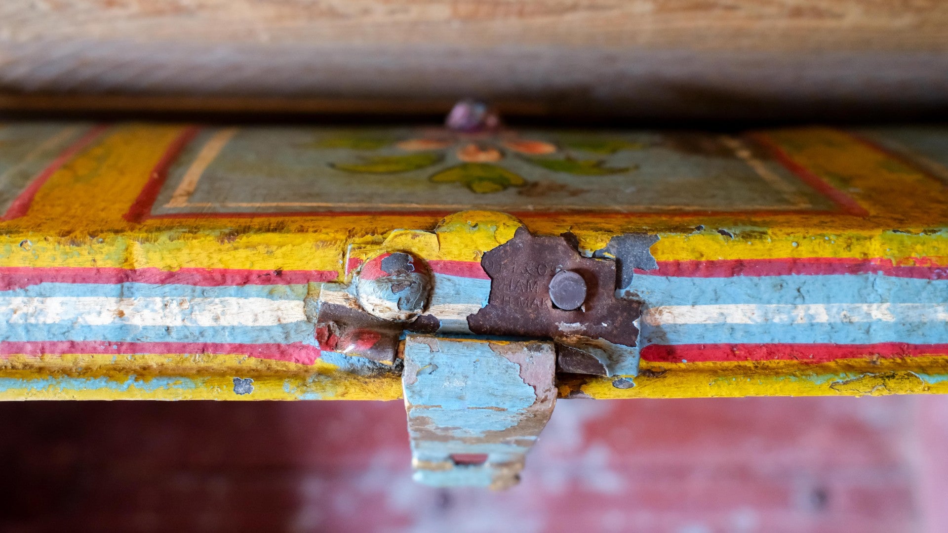Close-up of a rusty metal hinge on an old, colorful wooden surface.