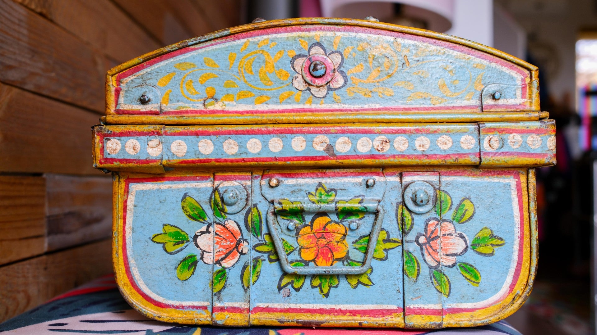 Colorful hand-painted metal box with floral designs on a blurred background