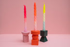 Three colorful candles on unique holders against a pink background