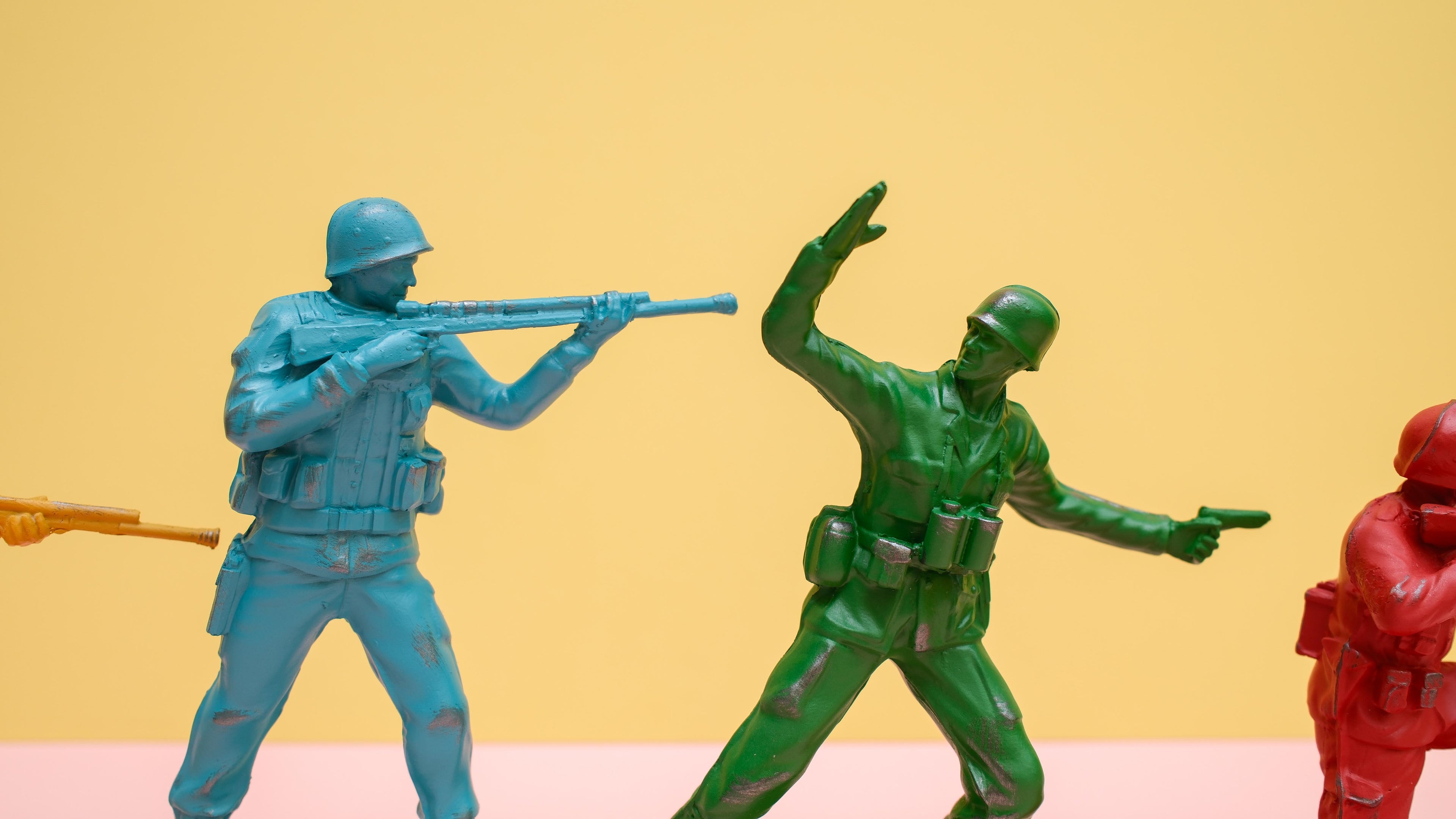 Toy soldiers in blue, green, and red on a yellow and pink background