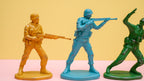 Three toy soldier figurines in yellow, blue, and green on a pink and yellow background