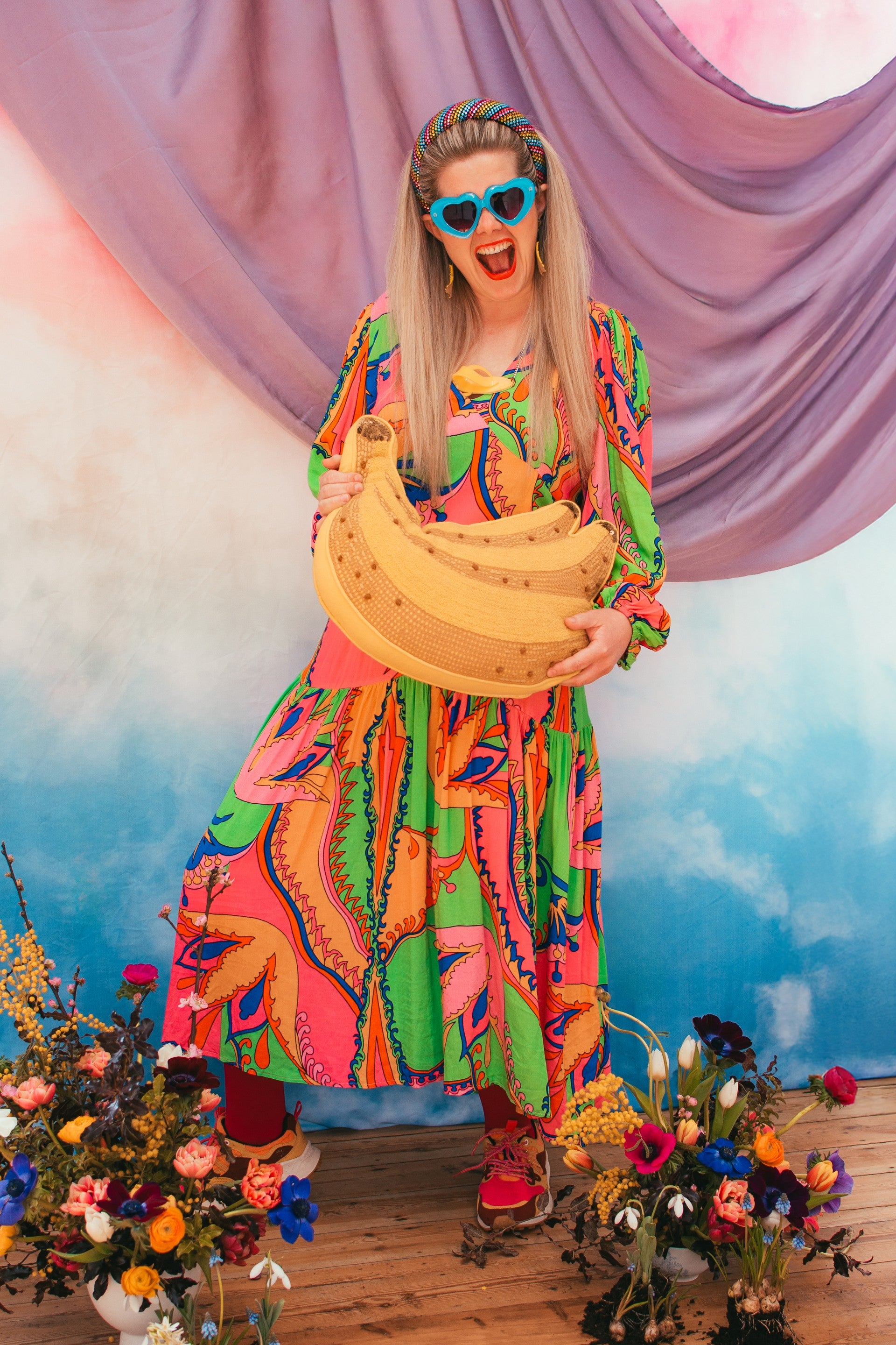 Person in a colorful outfit holding a large banana with a vibrant background