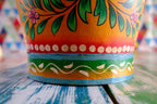 Colorful floral hand painted bucket on a table with a multicolored geometric patterned wall in the background
