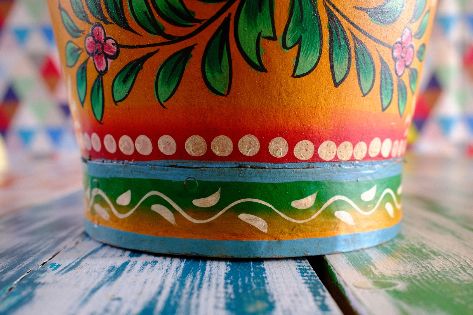 Colorful floral hand painted bucket on a table with a multicolored geometric patterned wall in the background