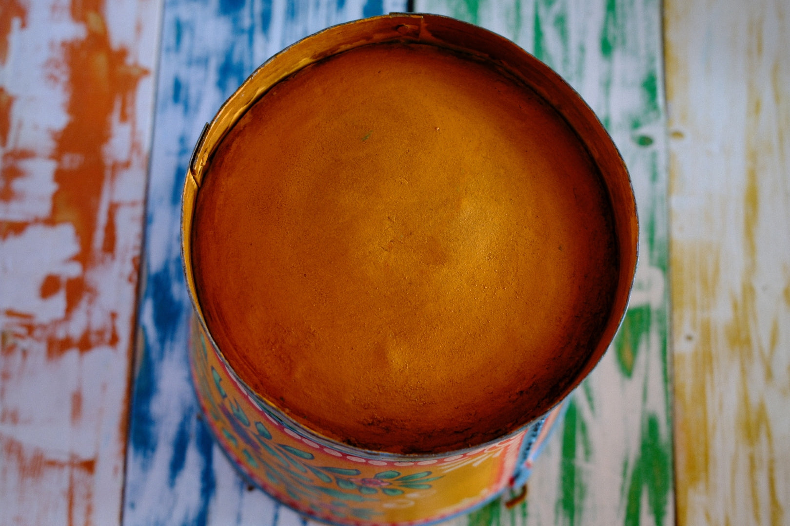 Colorful floral hand painted bucket on a table with a multicolored geometric patterned wall in the background