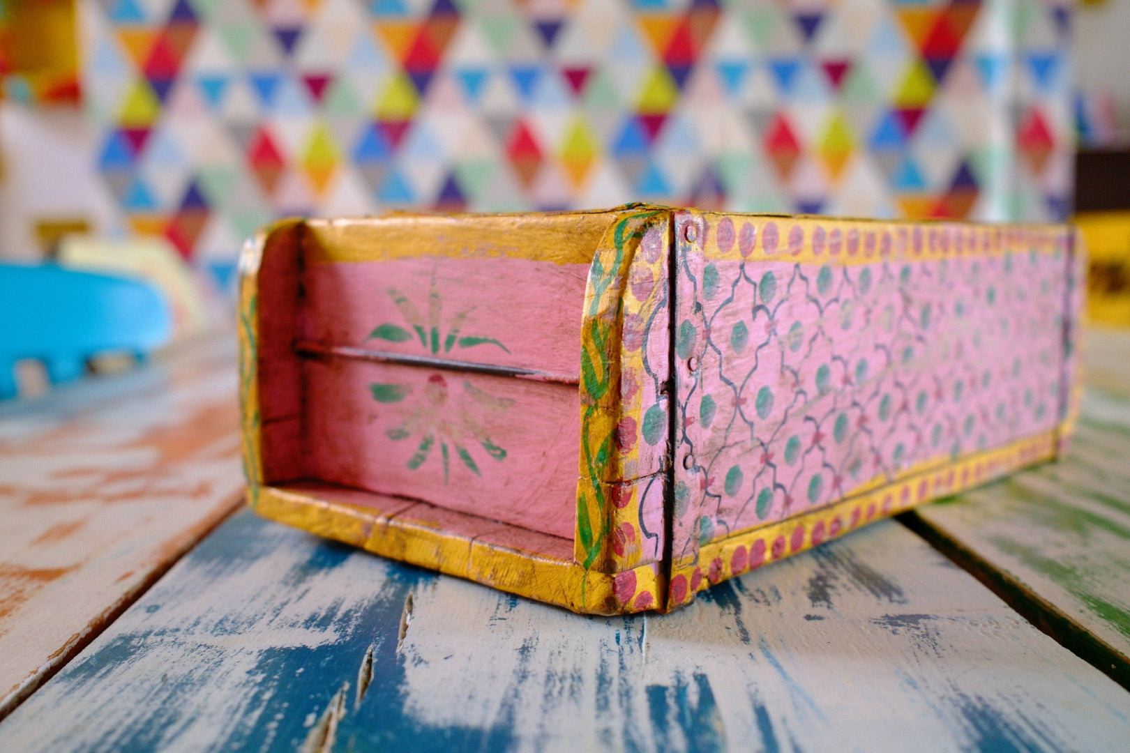 Pink box with colorful patterns on a wooden surface with a multicolored geometric pattern in the background.