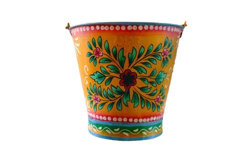 Colorful floral hand painted bucket on a table with a multicolored geometric patterned wall in the background