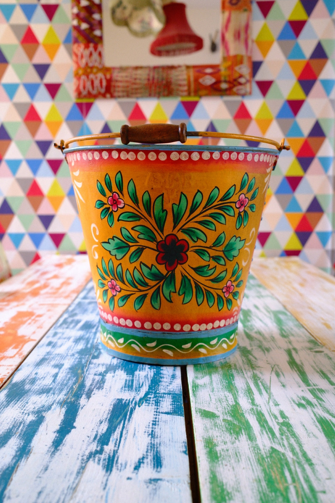 Colorful floral hand painted bucket on a table with a multicolored geometric patterned wall in the background