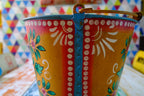 Decorative metal bucket with colorful patterns against a multicolored geometric background