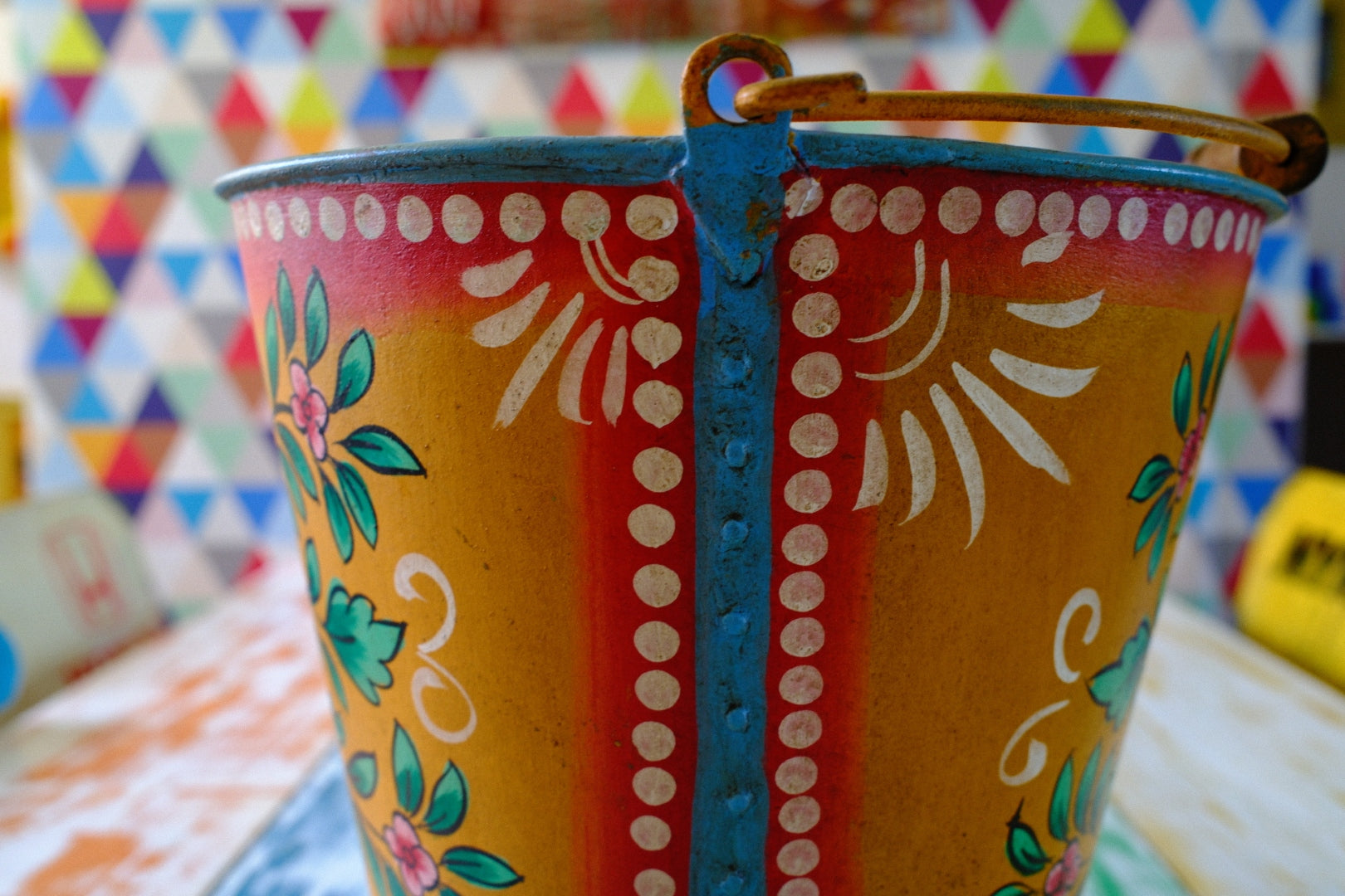 Decorative metal bucket with colorful patterns against a multicolored geometric background