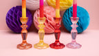 Colorful glass candlesticks with candles in front of colorful paper balls on a pink background