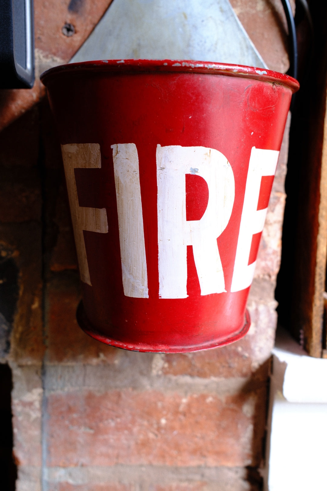 Red fire bucket with 'FIRE' written on it, leaning against a brick wall.