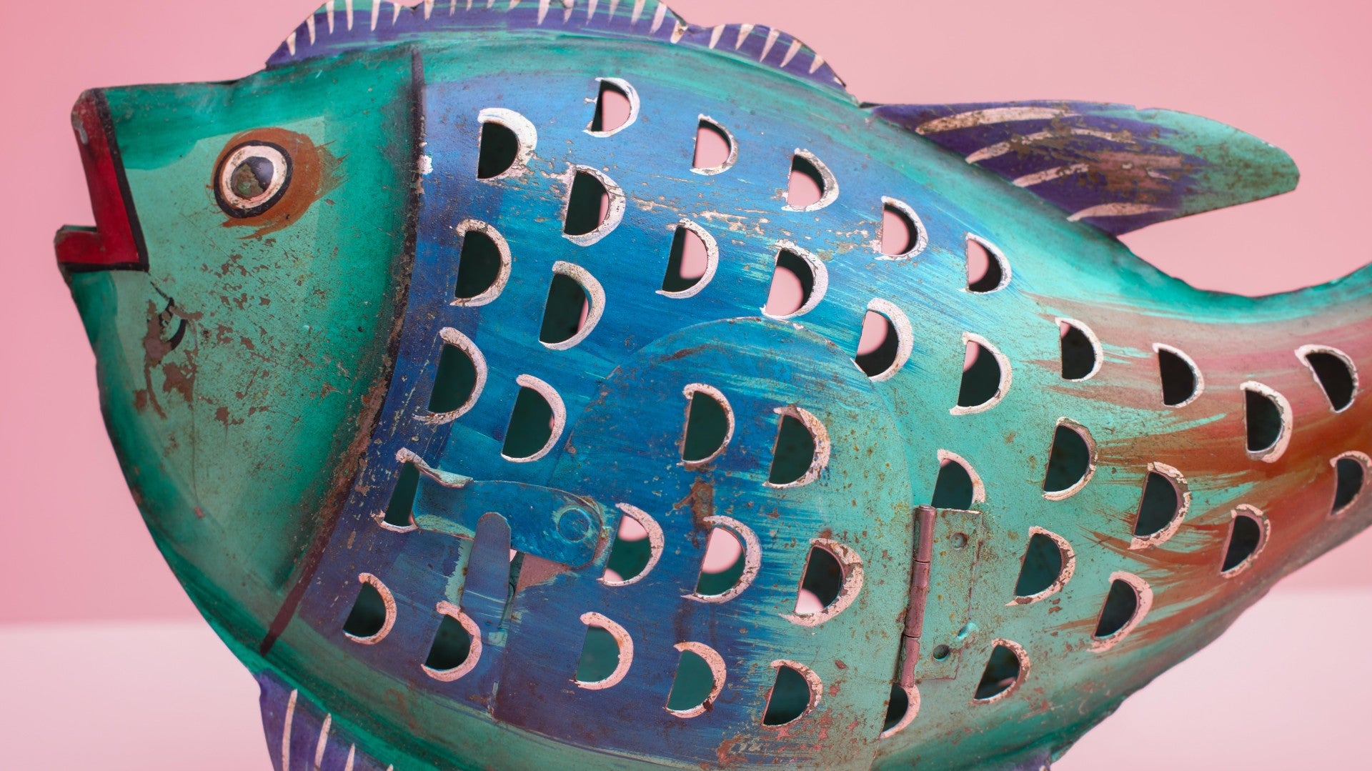 Decorative fish sculpture with teal and brown colors on a pink background