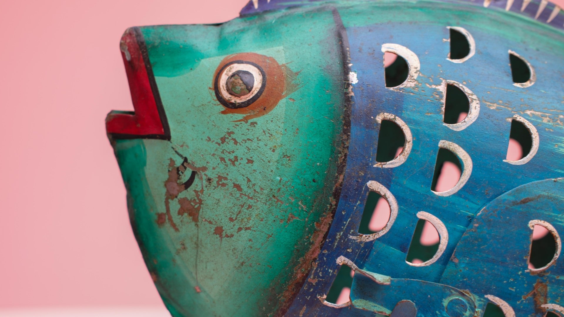 Vintage-style fish-shaped object with teal and blue colors on a pink background