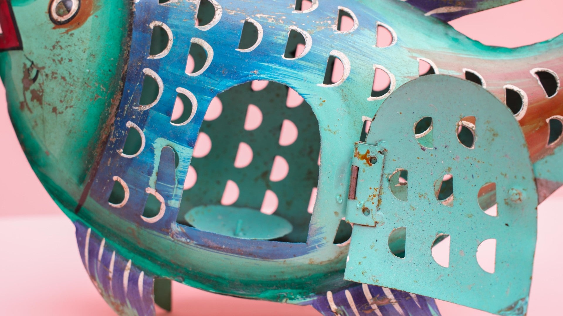 Close-up of a decorative metal fish with turquoise body and pink polka dot pattern on a pink background