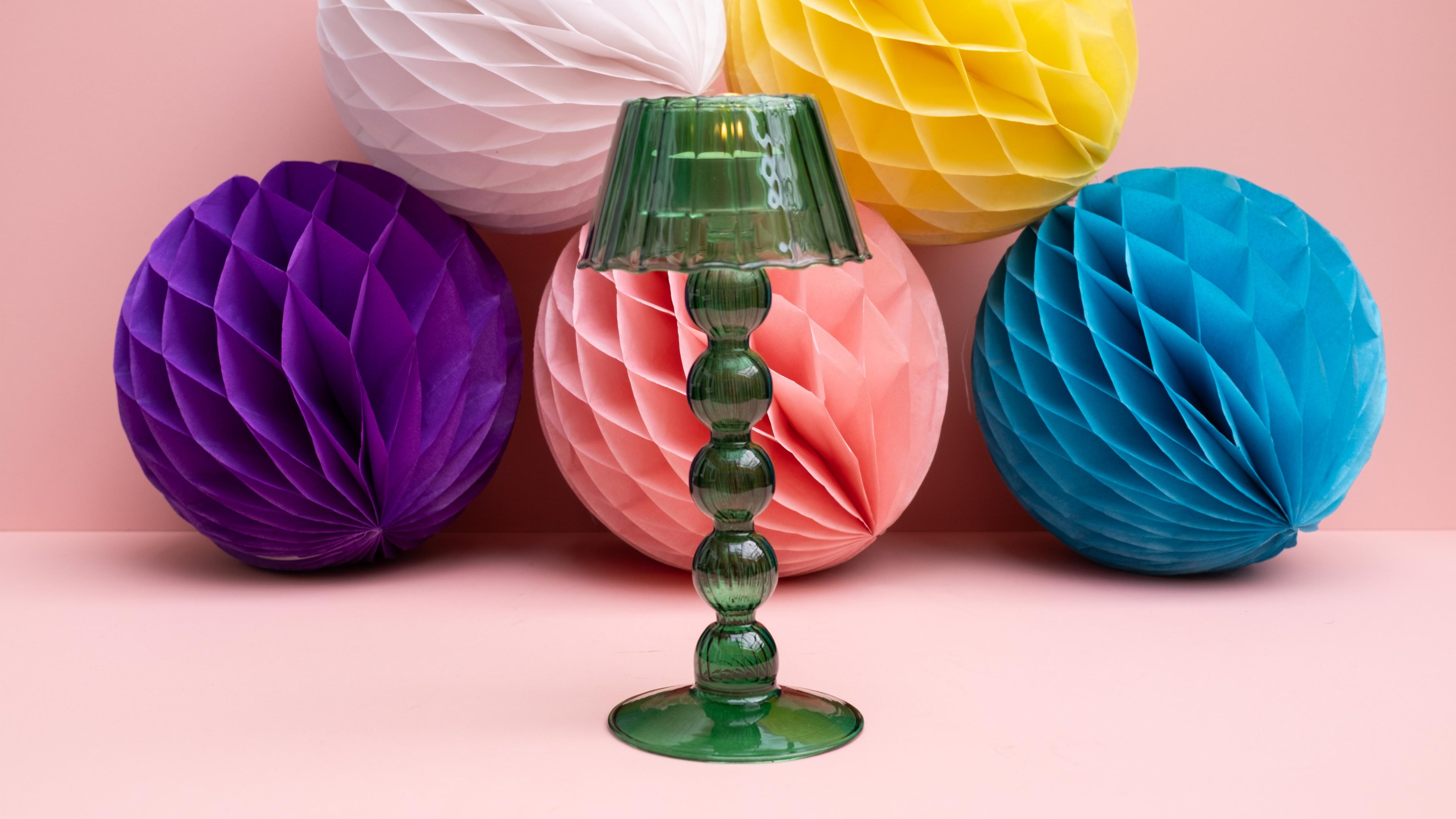 Green glass tealight lamp with colorful honeycomb balls on a pink background