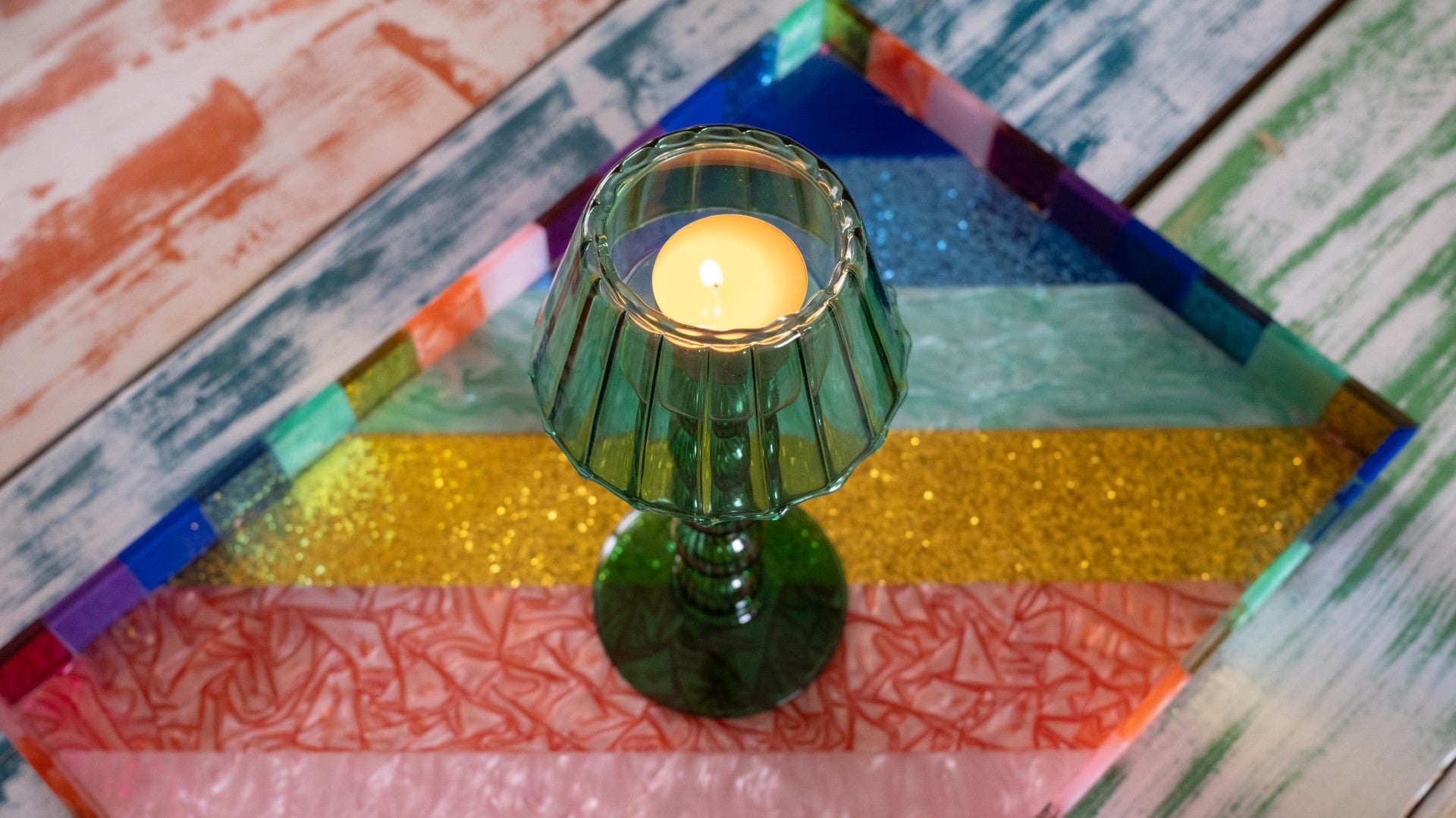 Green candle holder with a lit candle on a colorful, patterned surface