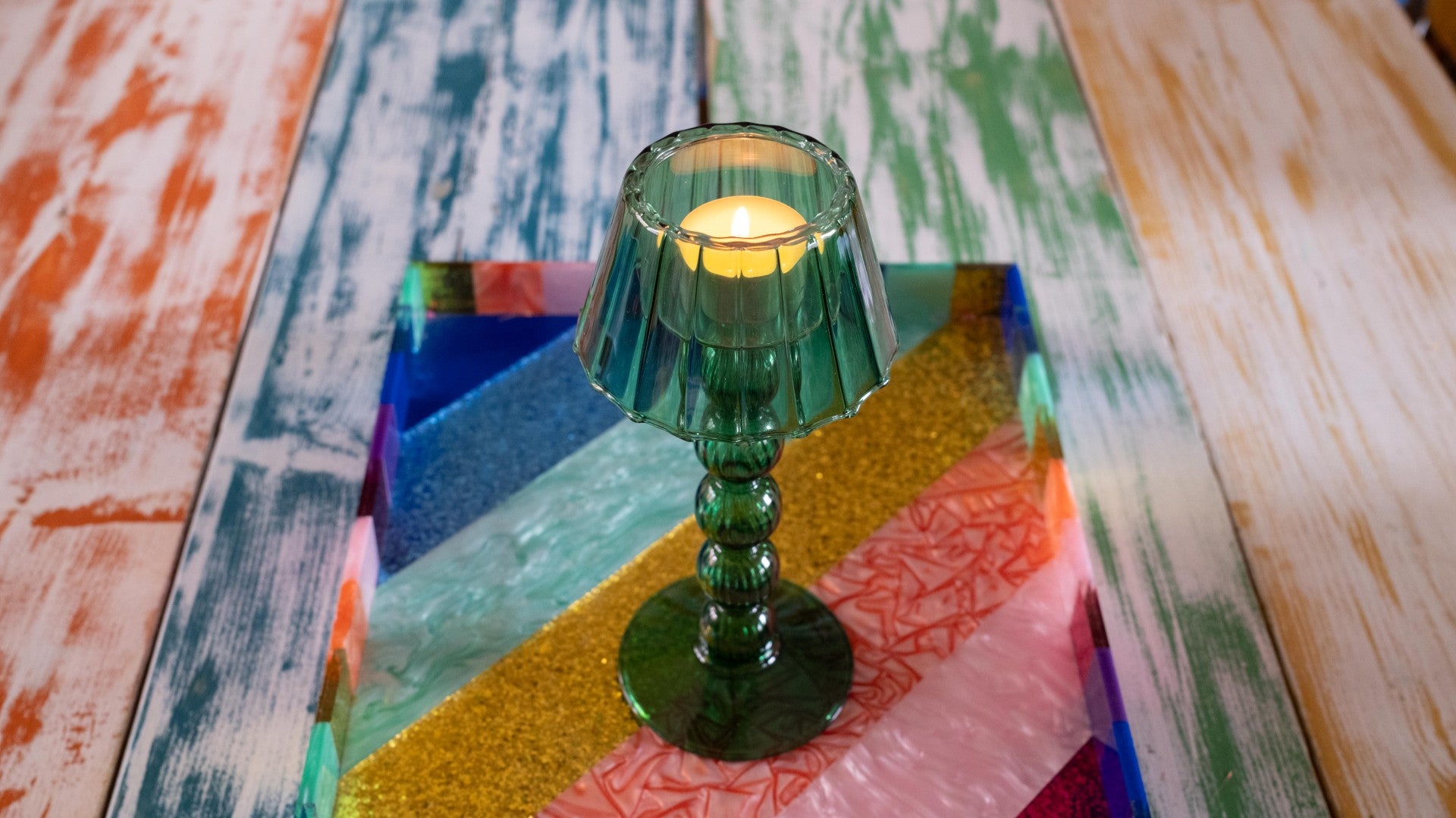 Green glass candle holder with a lit candle on a colorful wooden surface