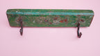 Green wooden wall hook with two metal hooks on a pink background