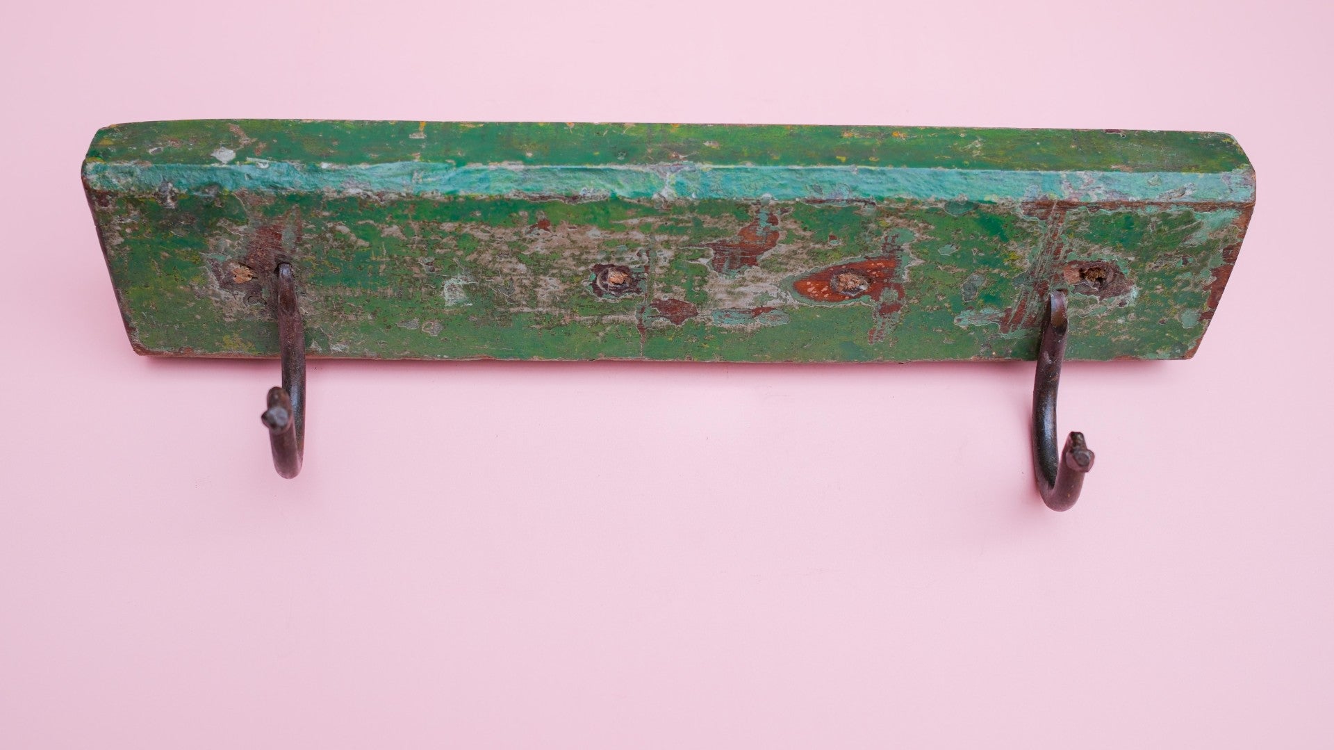 Green wooden wall hook with two metal hooks on a pink background
