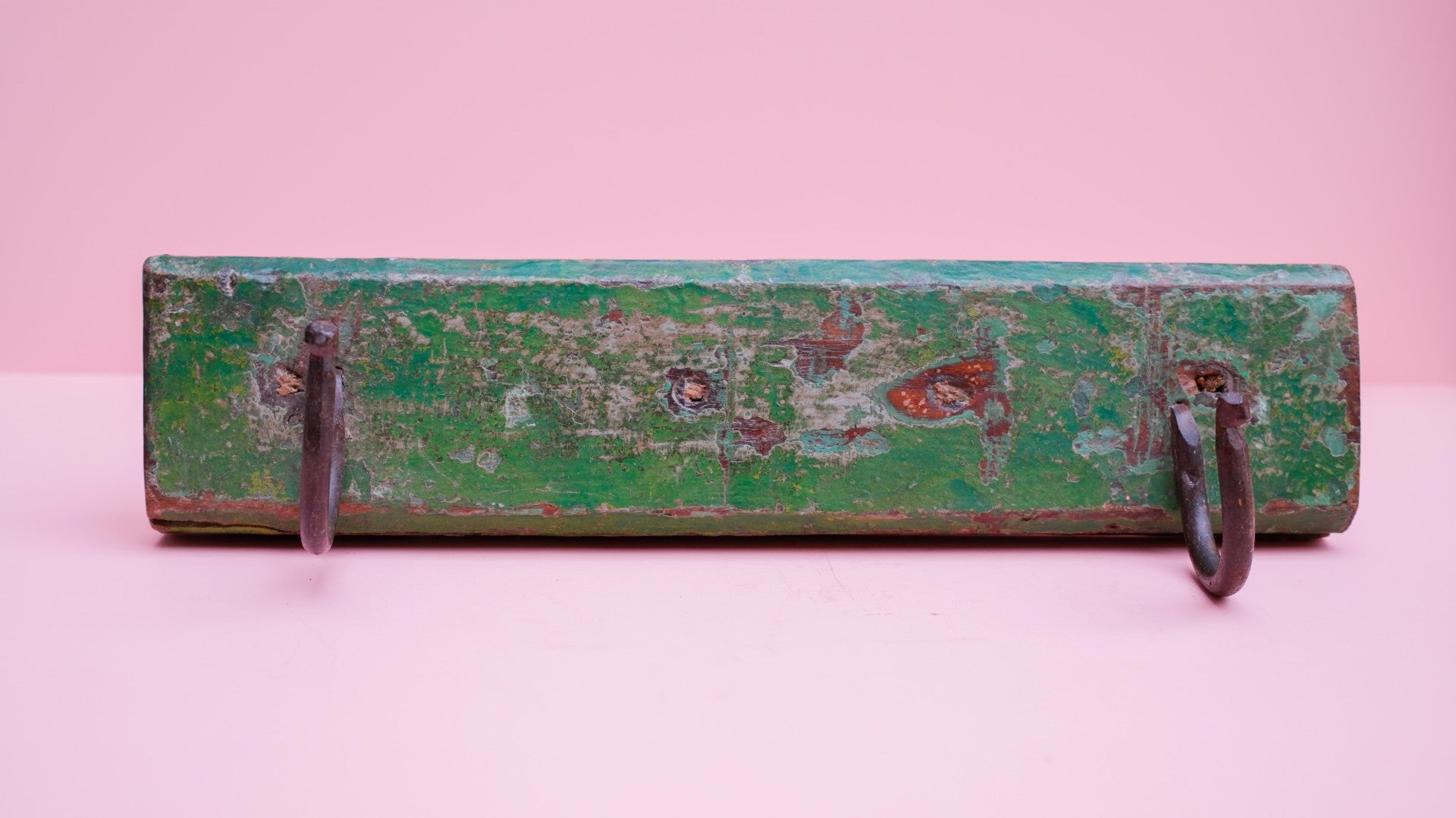 Vintage green metal tool box with two hooks on a pink background