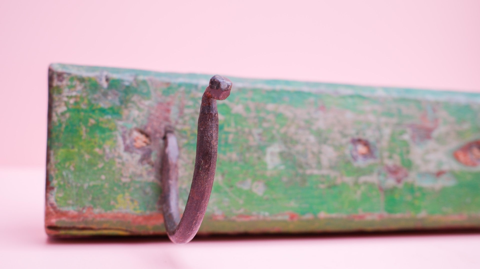 Hook on a green metal surface with a pink background