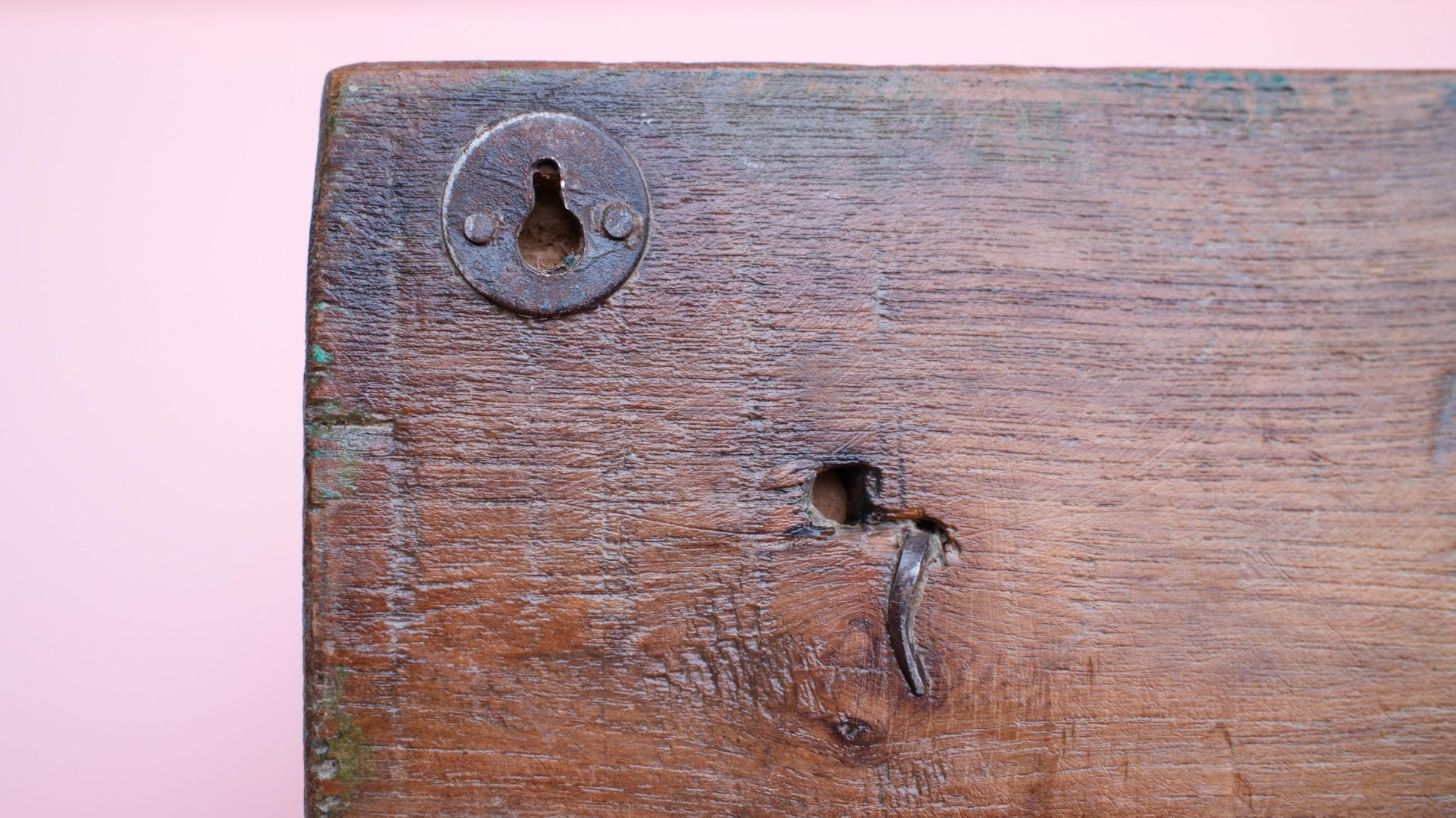 Close-up of an old wooden door with a lock and keyhole on a pink background