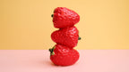 Stack of three strawberries on a pink and yellow gradient background