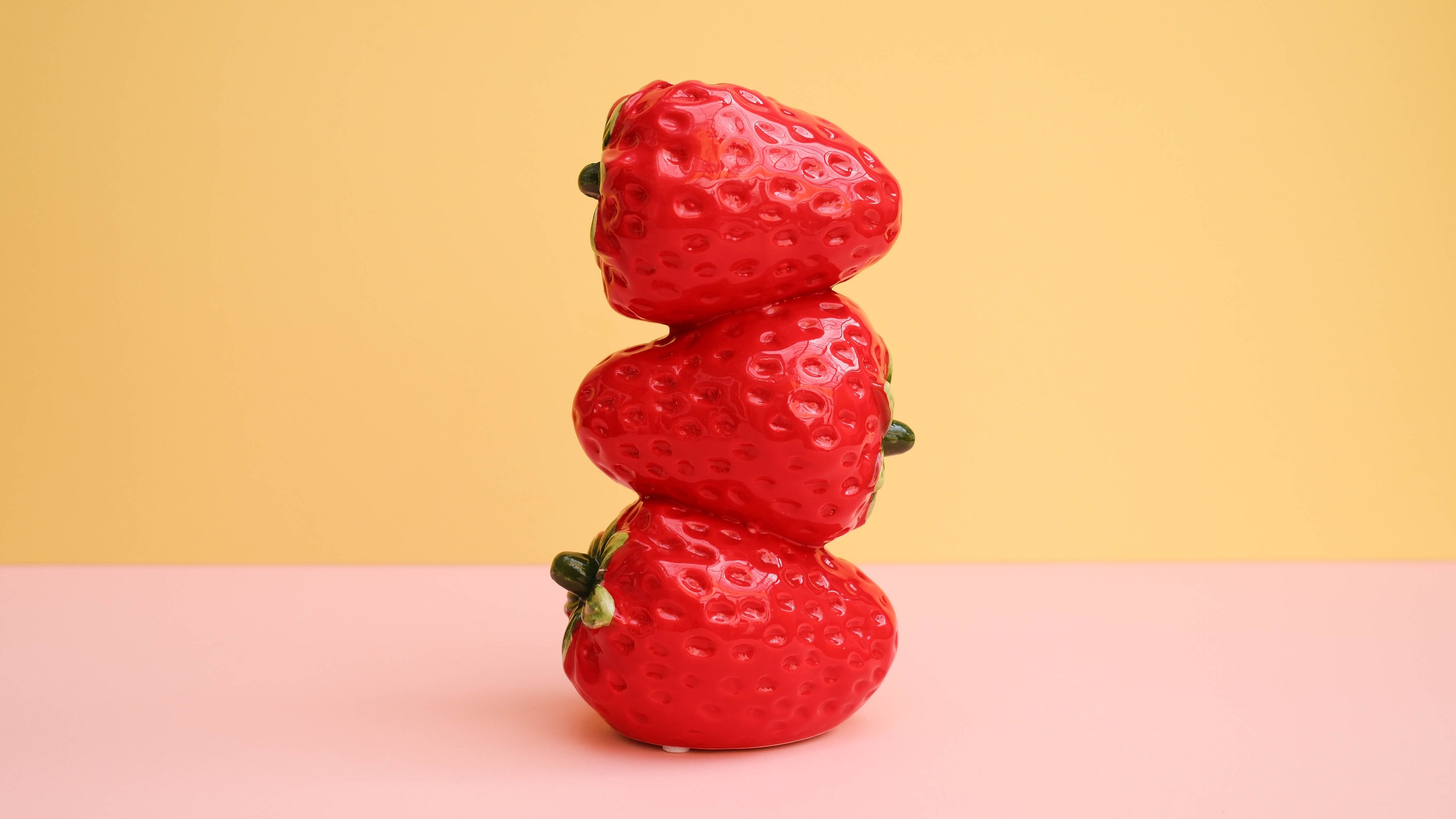 Stack of three strawberries on a pink and yellow gradient background