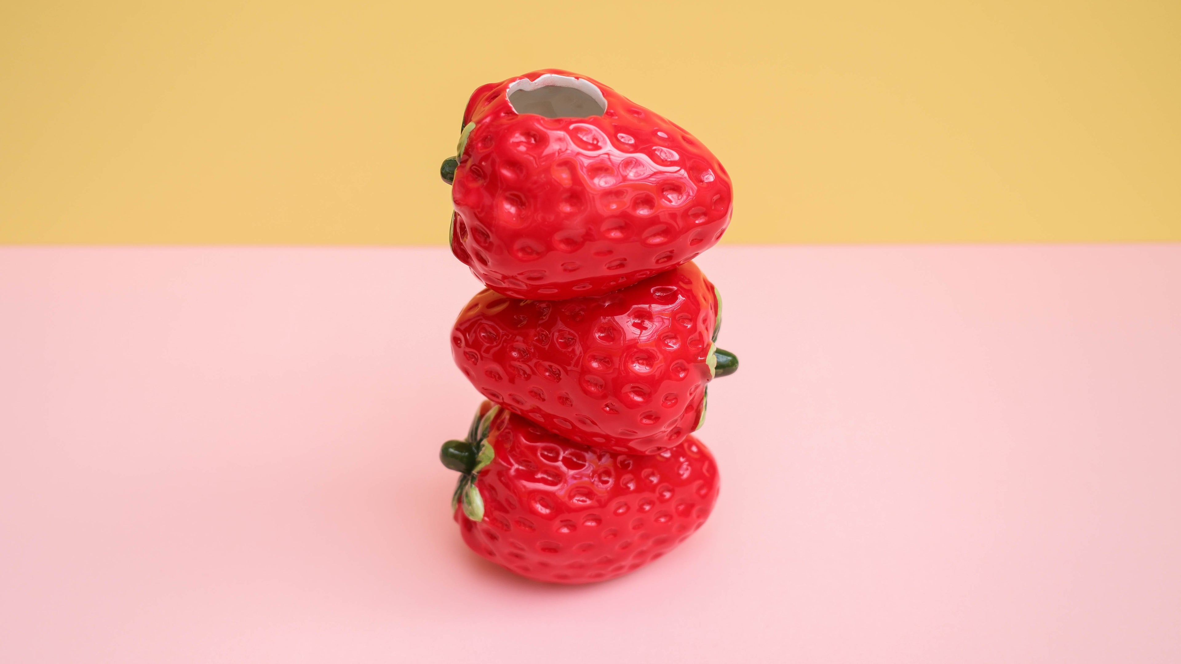 Stack of red strawberry-shaped objects on a pink and yellow gradient background