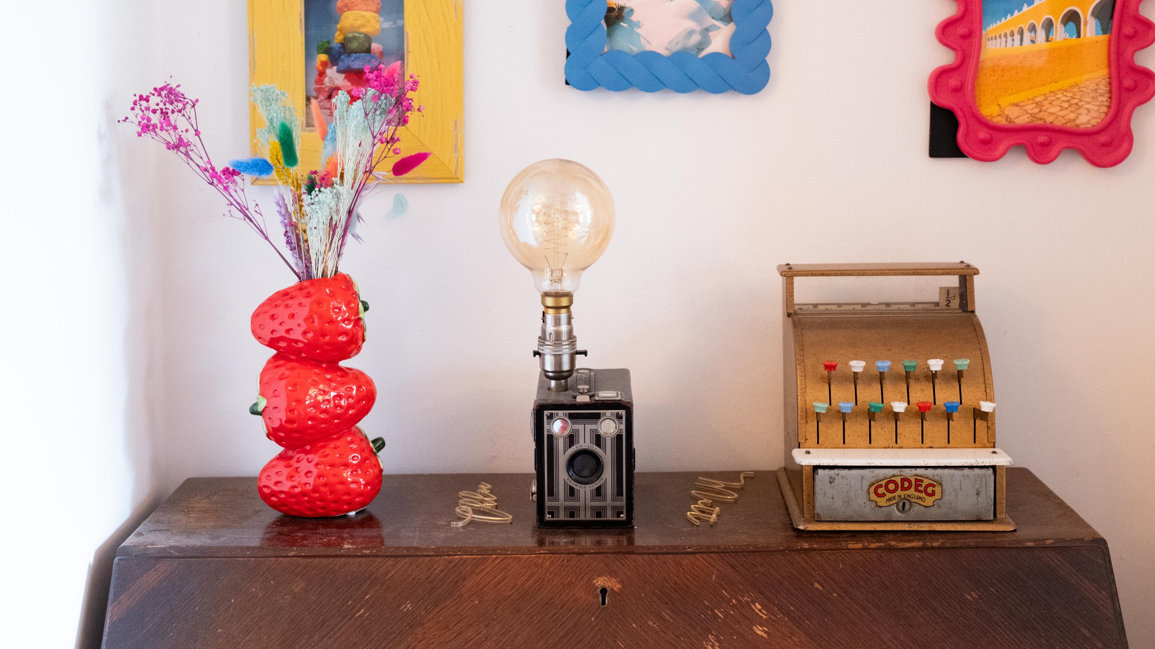 Decorative items including a strawberry vase with flowers, a vintage camera, and a small cash register on a wooden surface.