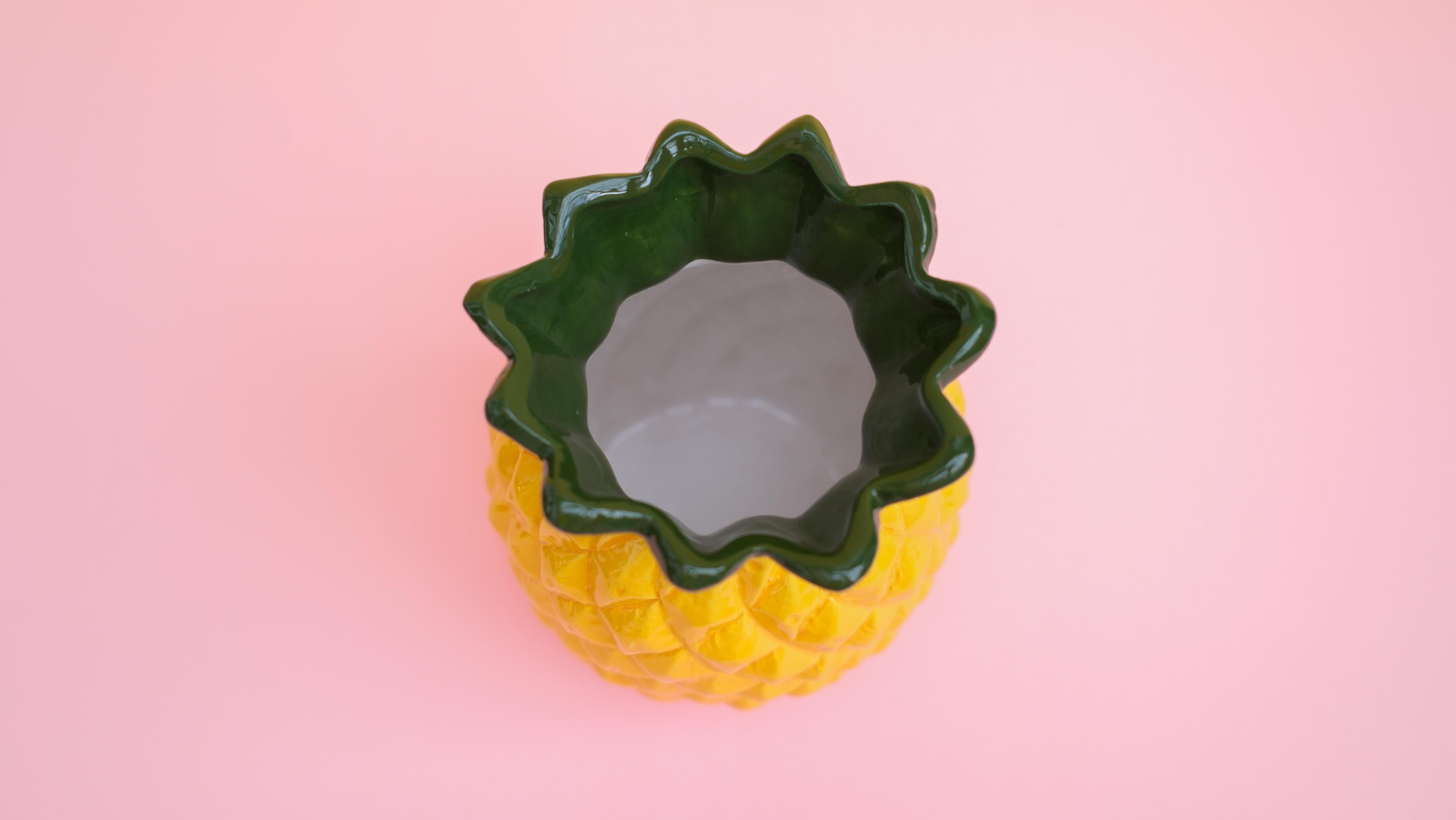 Pineapple-shaped container with green rim on a pink background