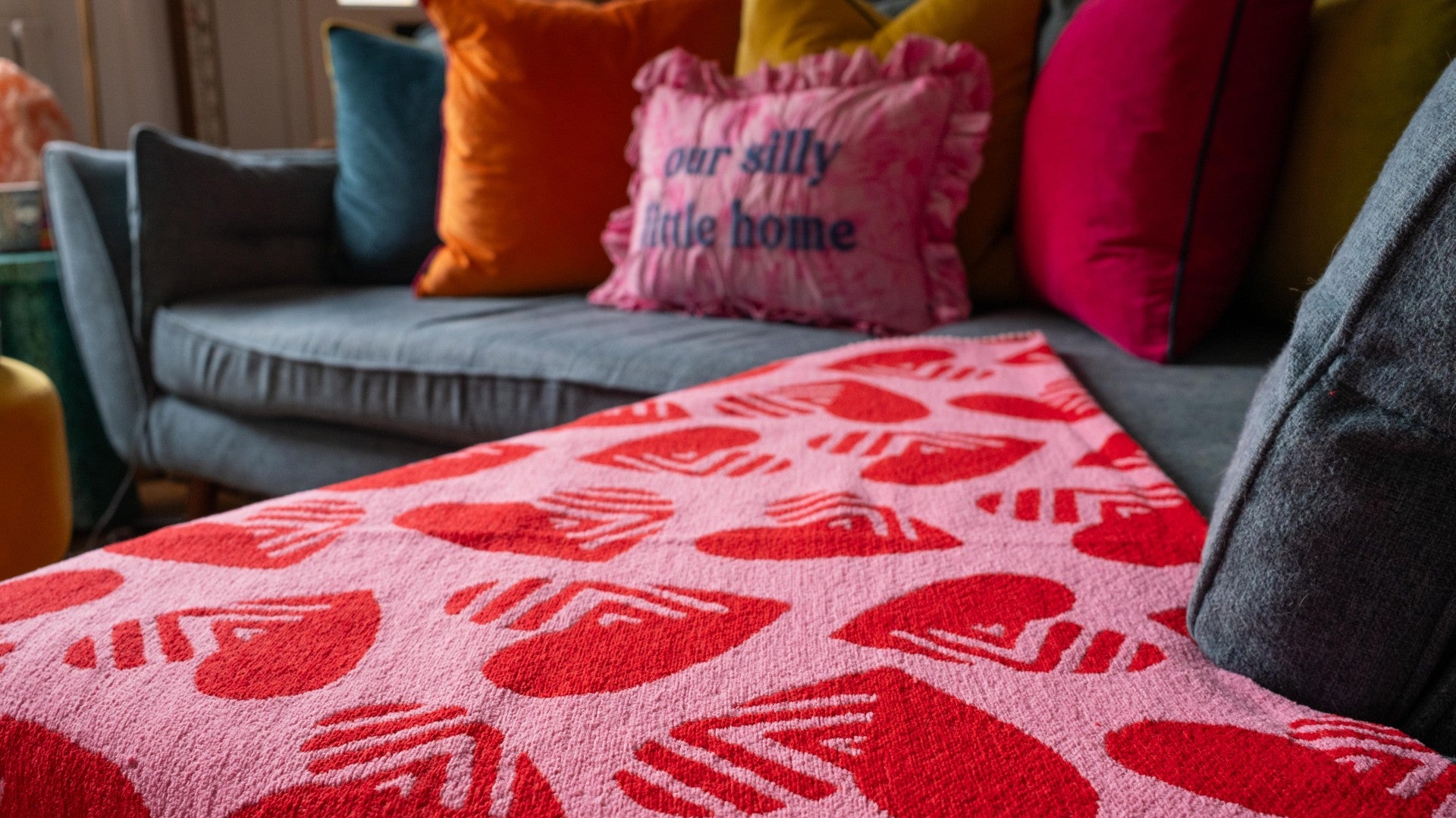 Colorful pillows on a couch with a red patterned blanket in the foreground.