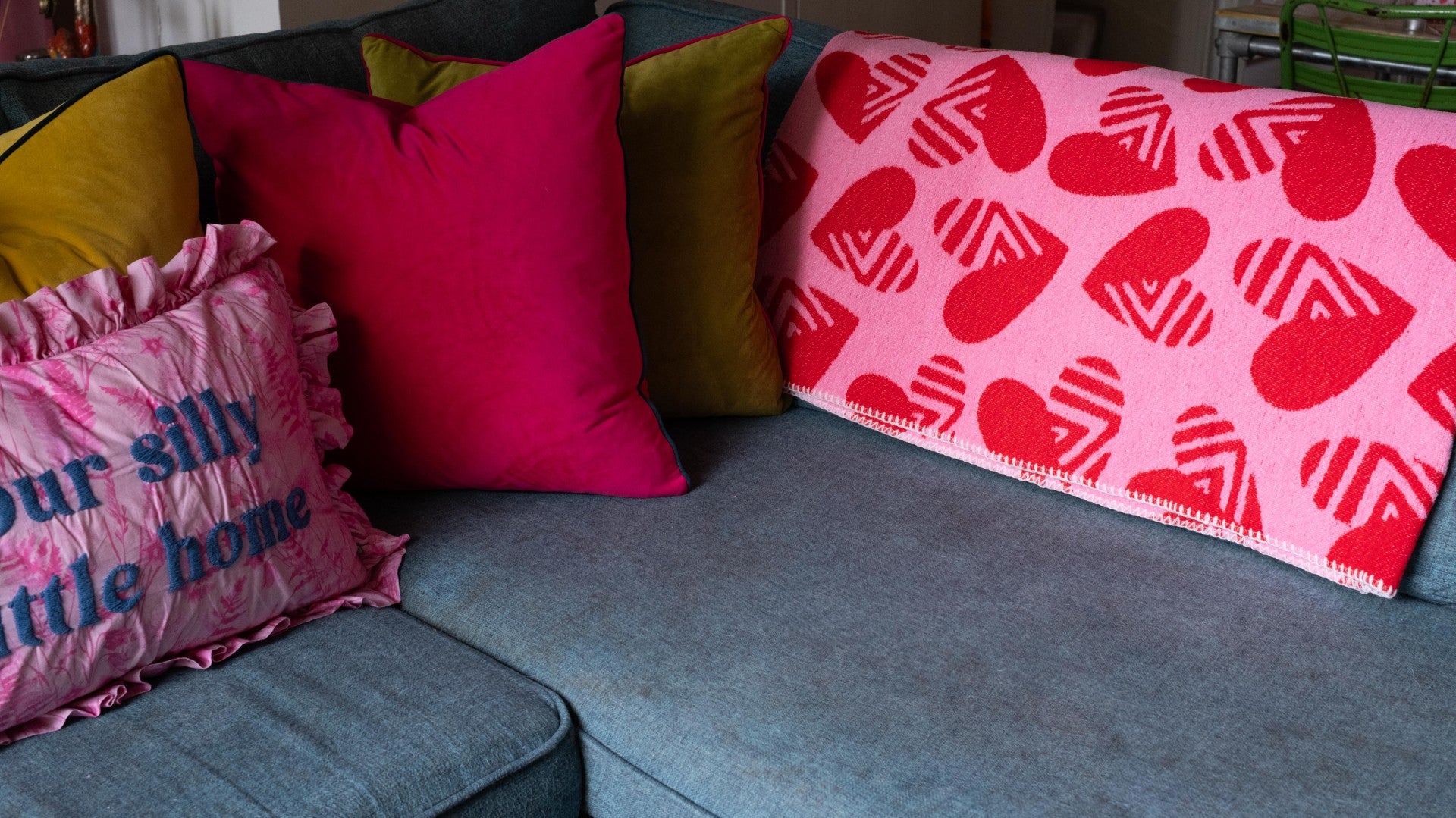 Sofa with colorful pillows and a blanket featuring red hearts on a blue couch.