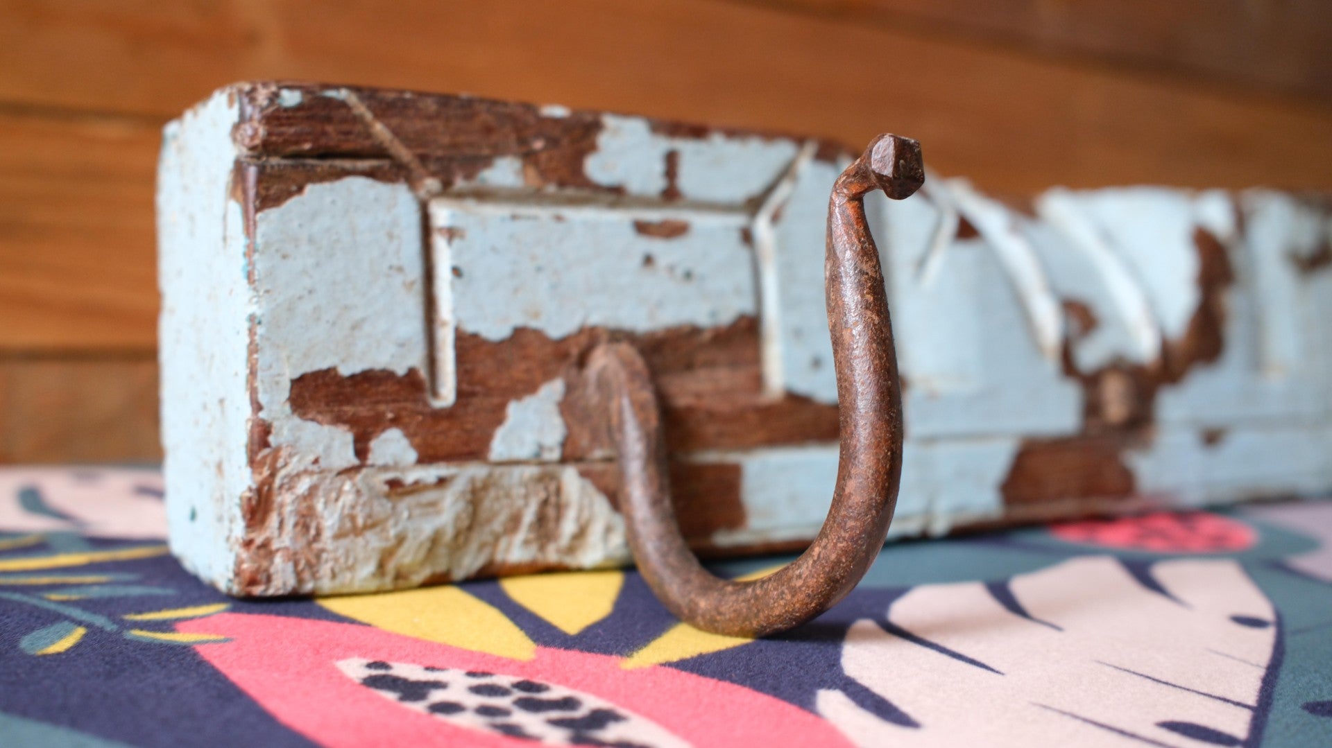 Rustic wooden hook with peeling paint on a colorful fabric background
