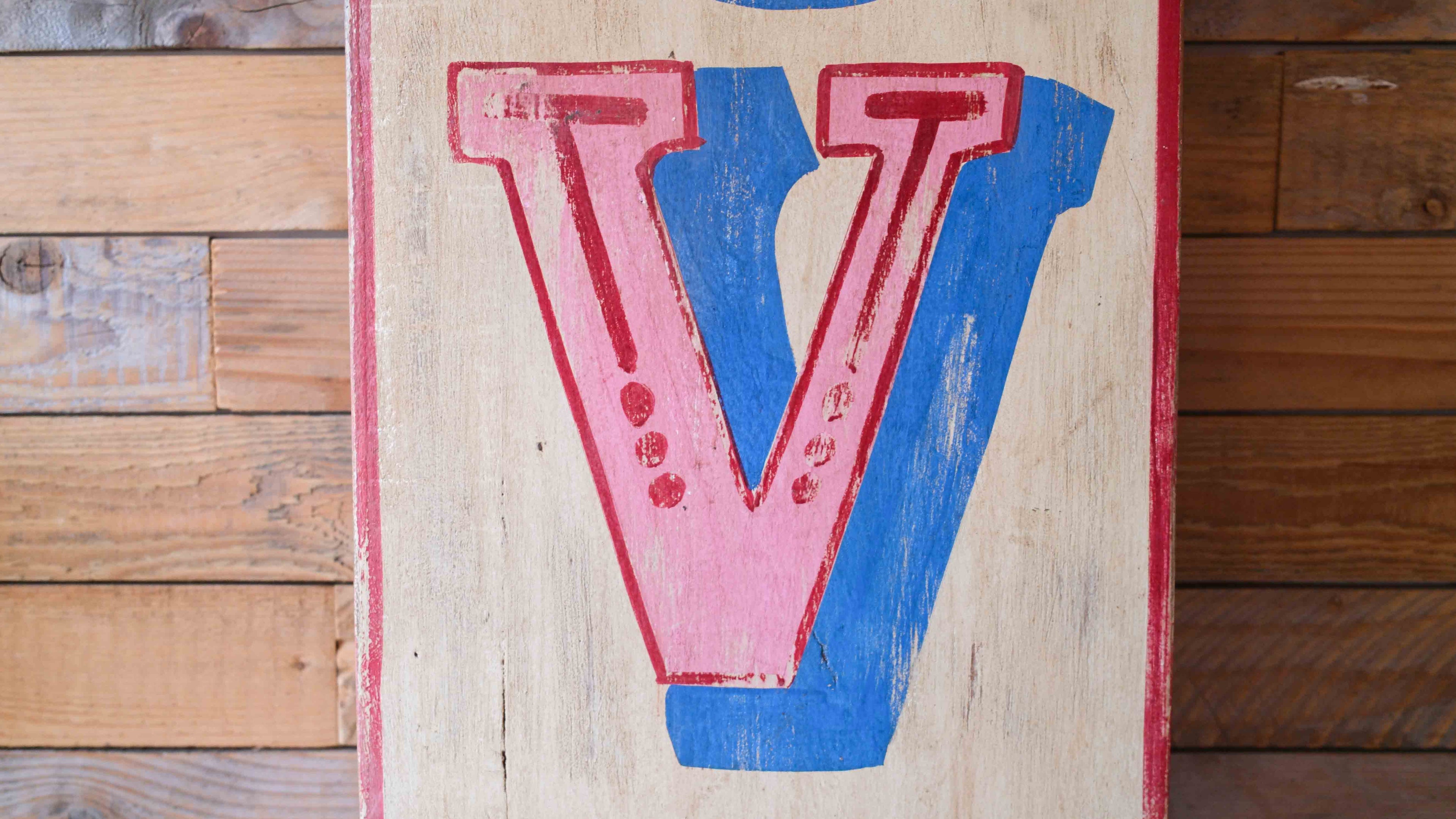 Wooden board with a large pink and blue letter 'V' on a wooden background