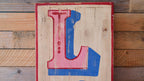 Wooden sign with a large red and blue letter 'L' on a wooden background