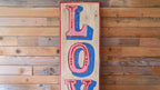 Wooden sign with 'LOVE' in red and blue on a wooden wall.