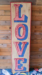 Wooden sign with 'LOVE' in red and blue letters against a wooden background