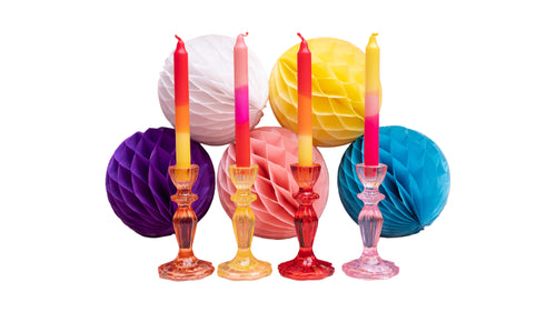 Colorful candles in glass candlesticks with decorative paper balls on a pink background