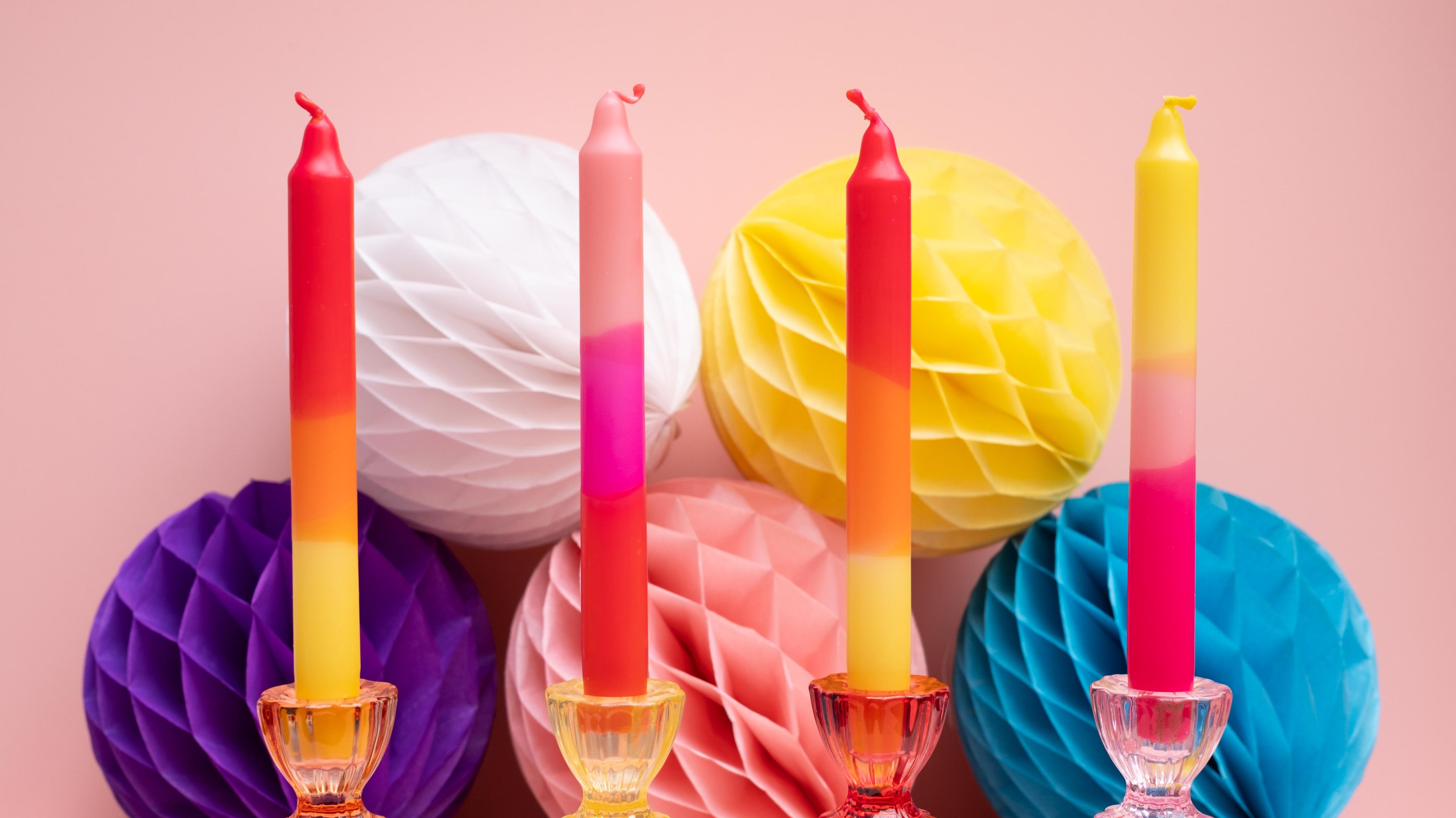 Colorful dinner candles and paper lanterns on a pink background