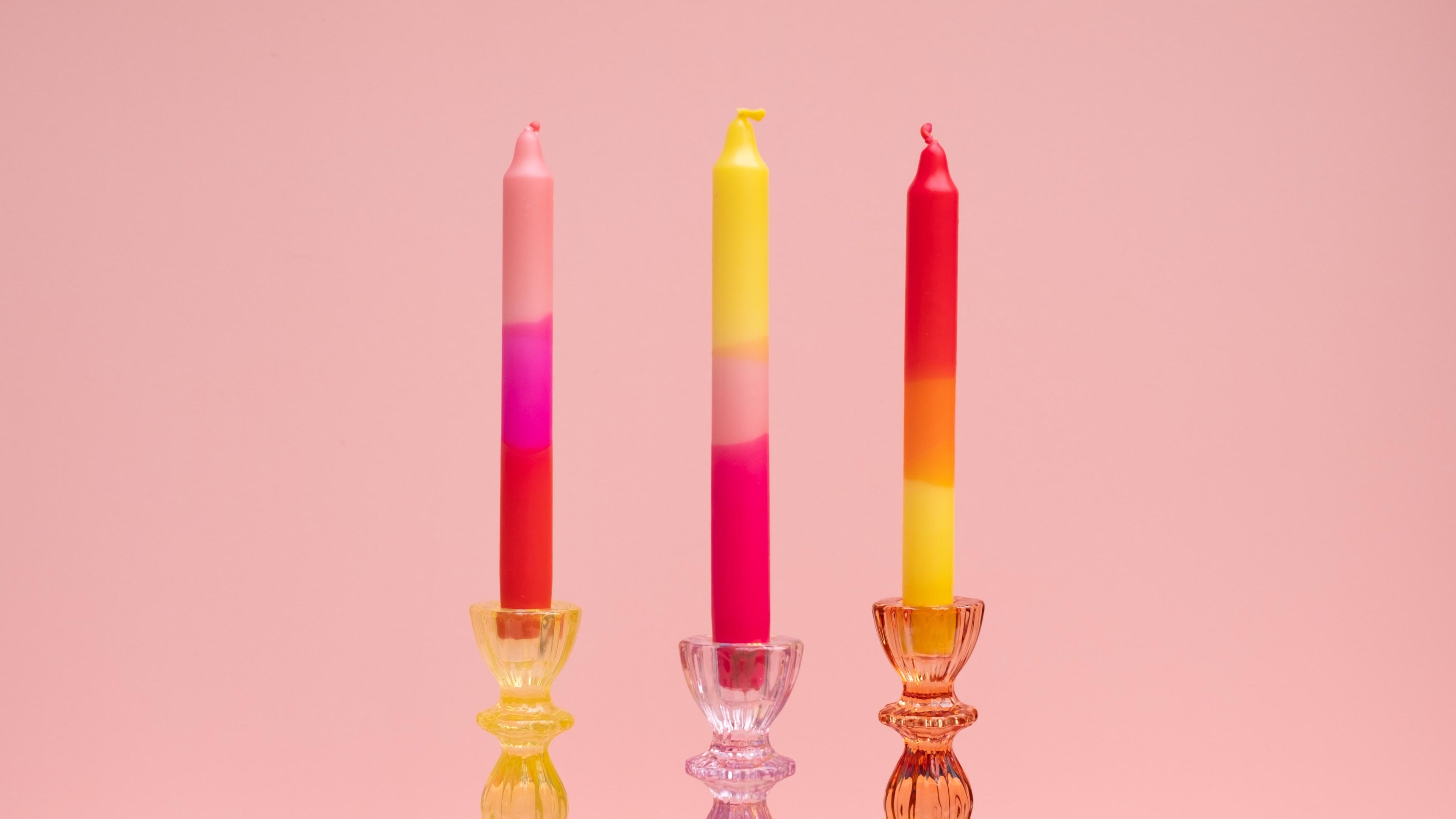 Three colorful candles with gradient hues on a pink background