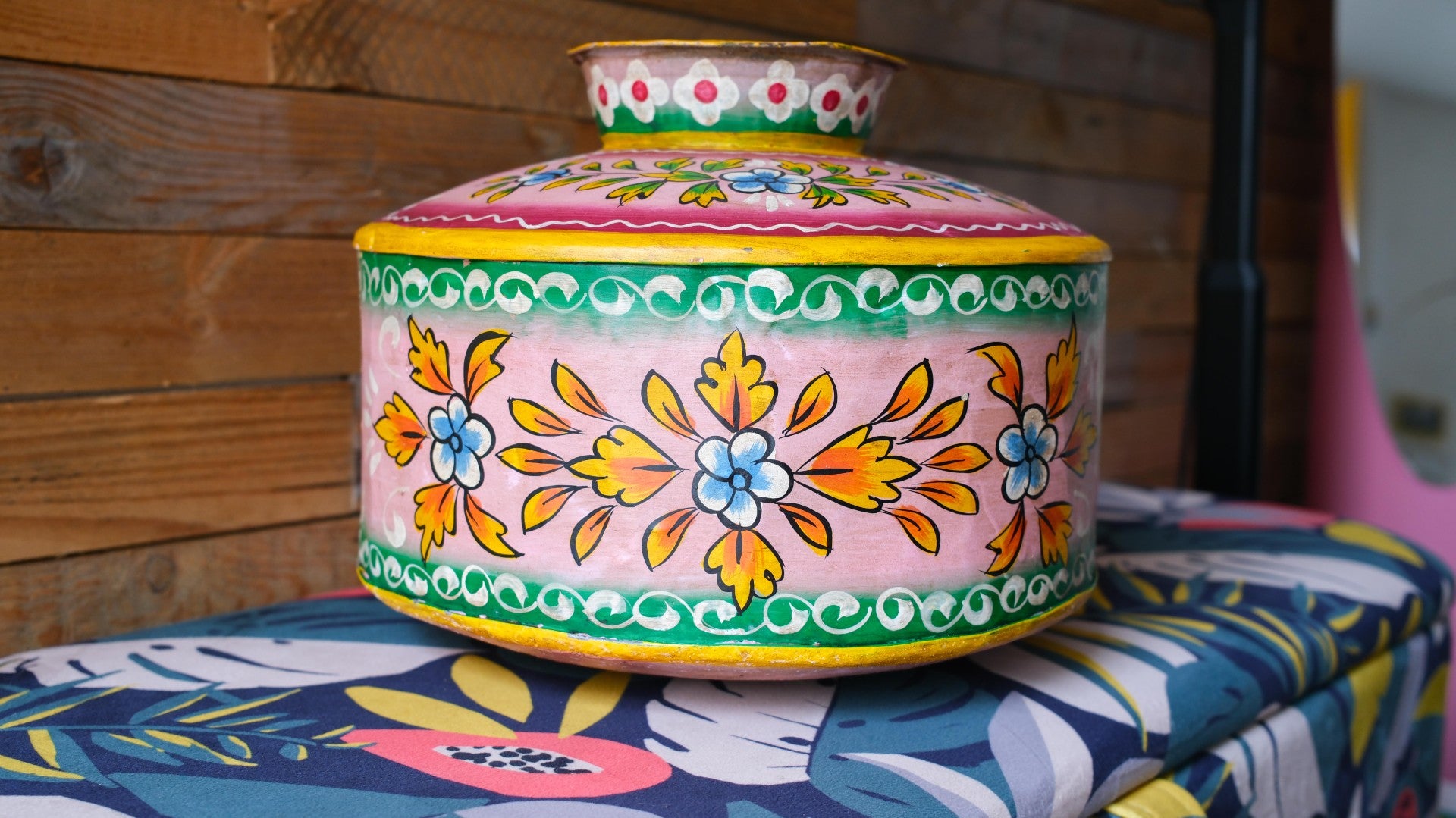Colorful metal pot with floral patterns on a patterned surface