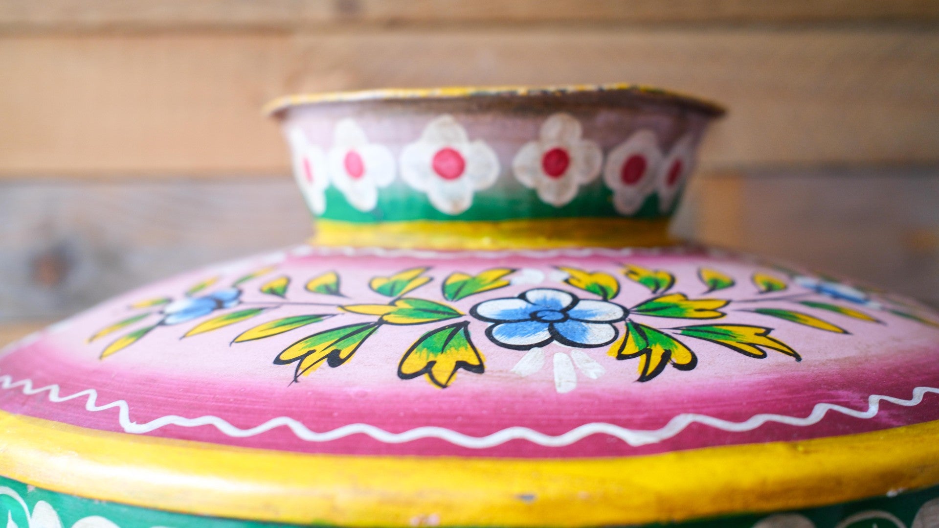 Colorful metal pot with floral patterns on a wooden surface