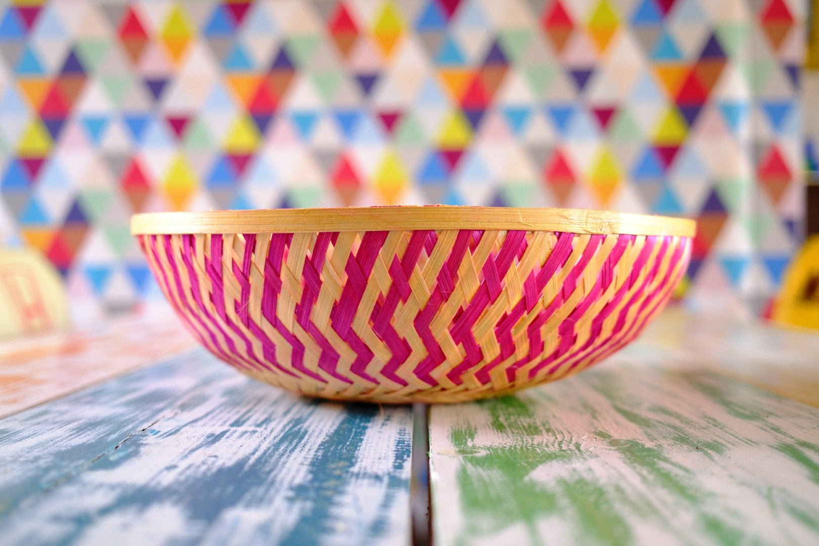Colorful woven basket with pink and yellow pattern on a table with a multicolored geometric background