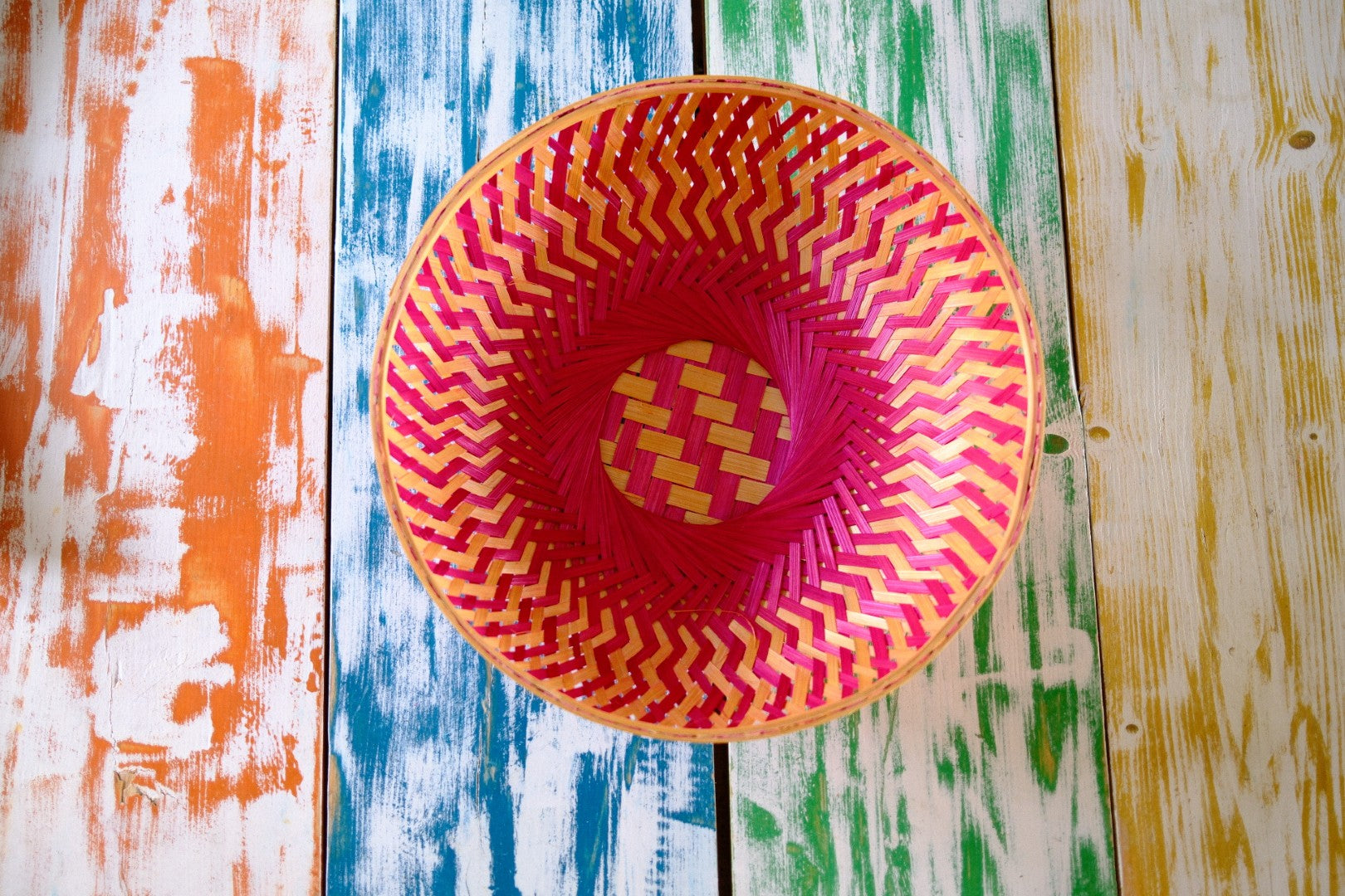 Colorful woven basket with pink and yellow pattern on a multicolored wooden surface
