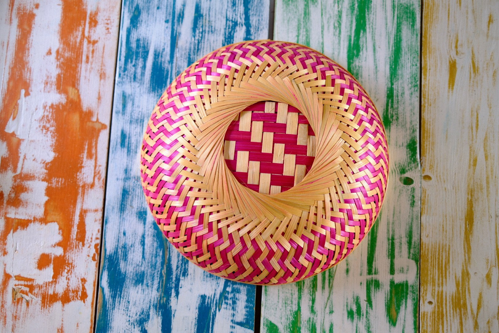 Woven basket with pink and yellow pattern on a colorful wooden surface