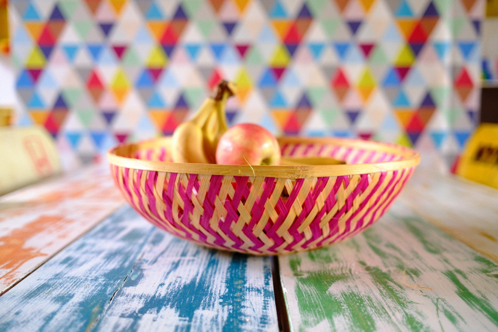 Decorative pink and yellow bowl with fruit on a colorful wooden table