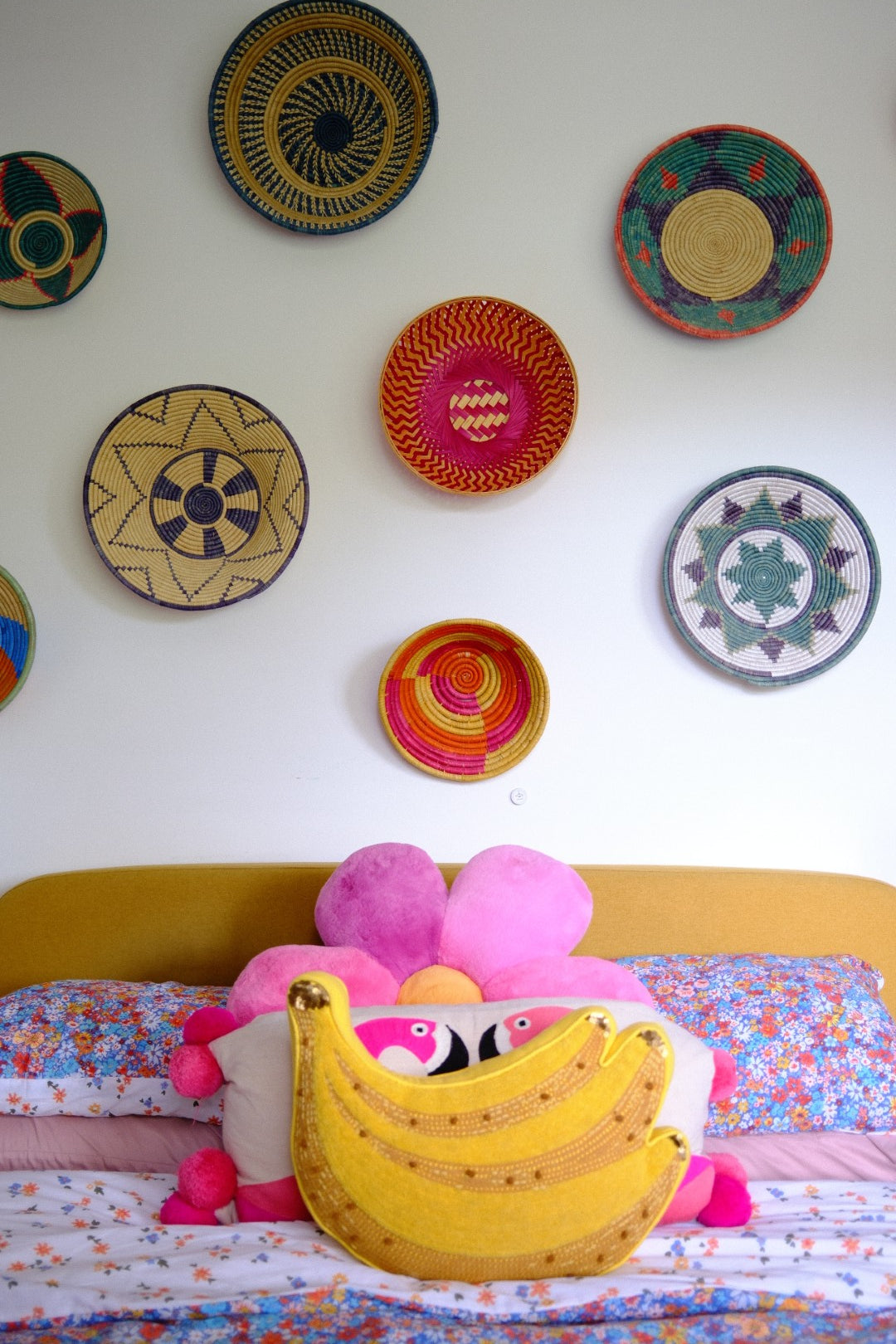 Colorful woven plates on a white wall with a floral curtain and pink plush floral cushion 